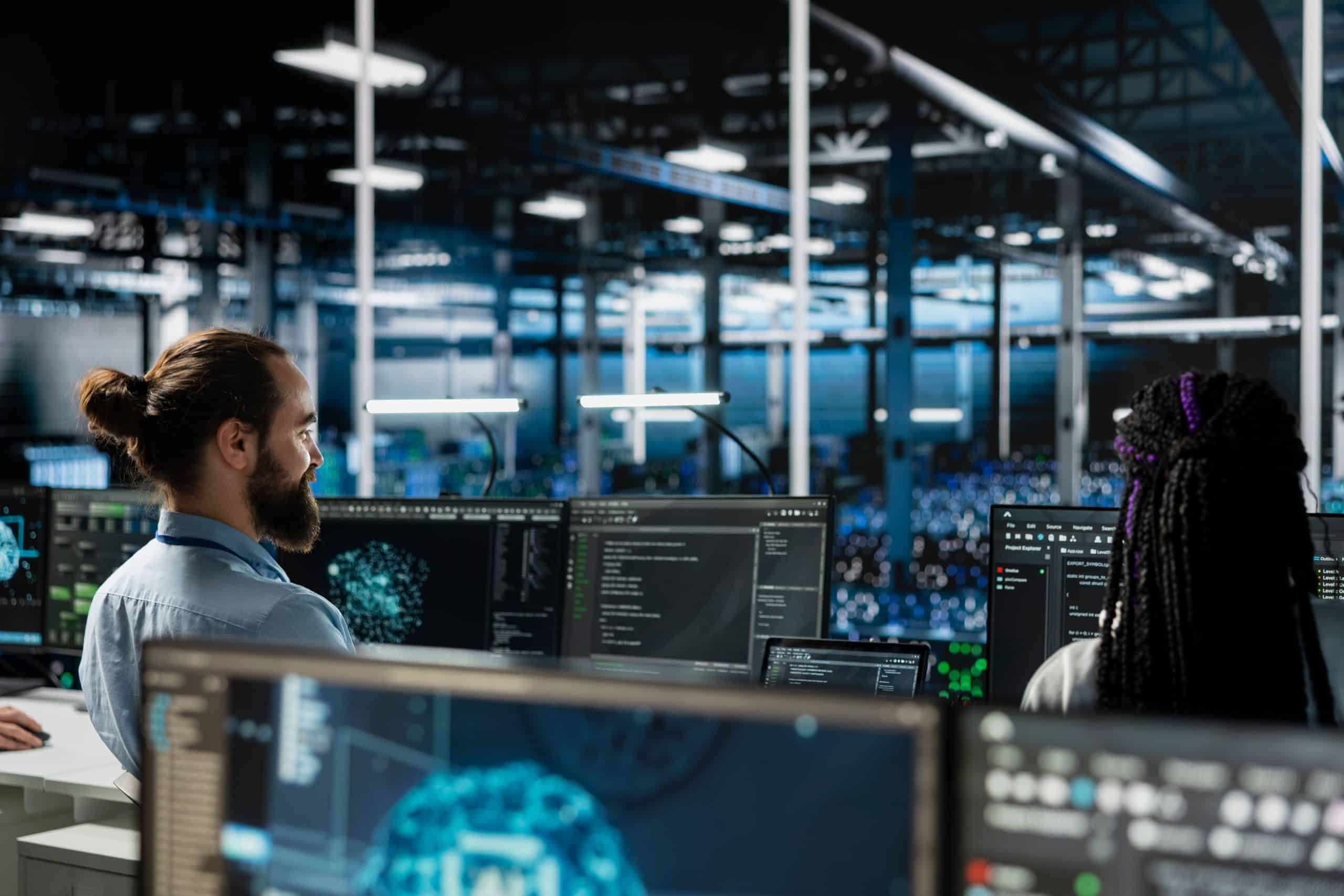 Zwei Personen arbeiten in einem modernen Büro an Computermonitoren, auf denen komplexe Daten und Grafiken angezeigt werden, umgeben von Hightech-Geräten und großen Fenstern mit Blick auf einen geschäftigen Hightech-Arbeitsplatz.